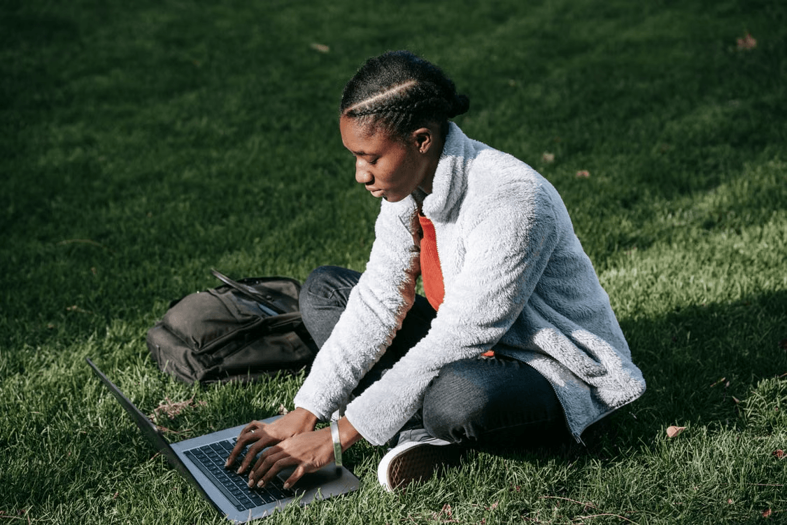 Student working on a laptop while sitting outdoors on the grass